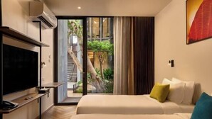 Une chambre d’hôtel équipée d’une télévision, d’un lit avec des oreillers et d’une porte-fenêtre coulissante donnant sur un balcon avec vue sur un escalier et de la verdure.