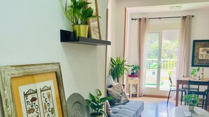A living room with a sofa, a small table, and a wall-mounted shelf with plants and framed artwork. - Atico Duplex 4 Habitaciones 3 Terrazas Vista 360° (Barcelona)