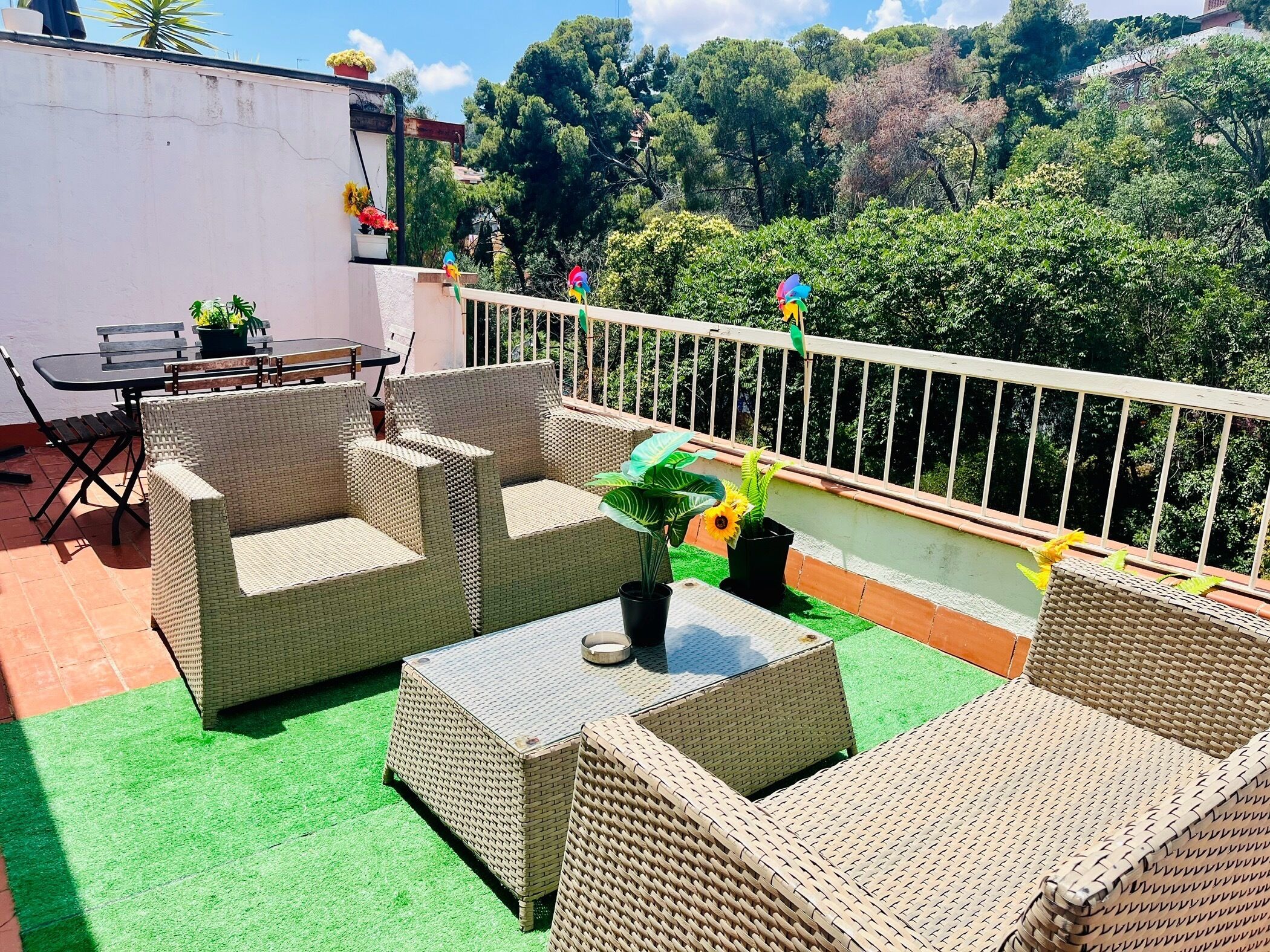 A rooftop terrace with wicker furniture, a small table, and potted plants.