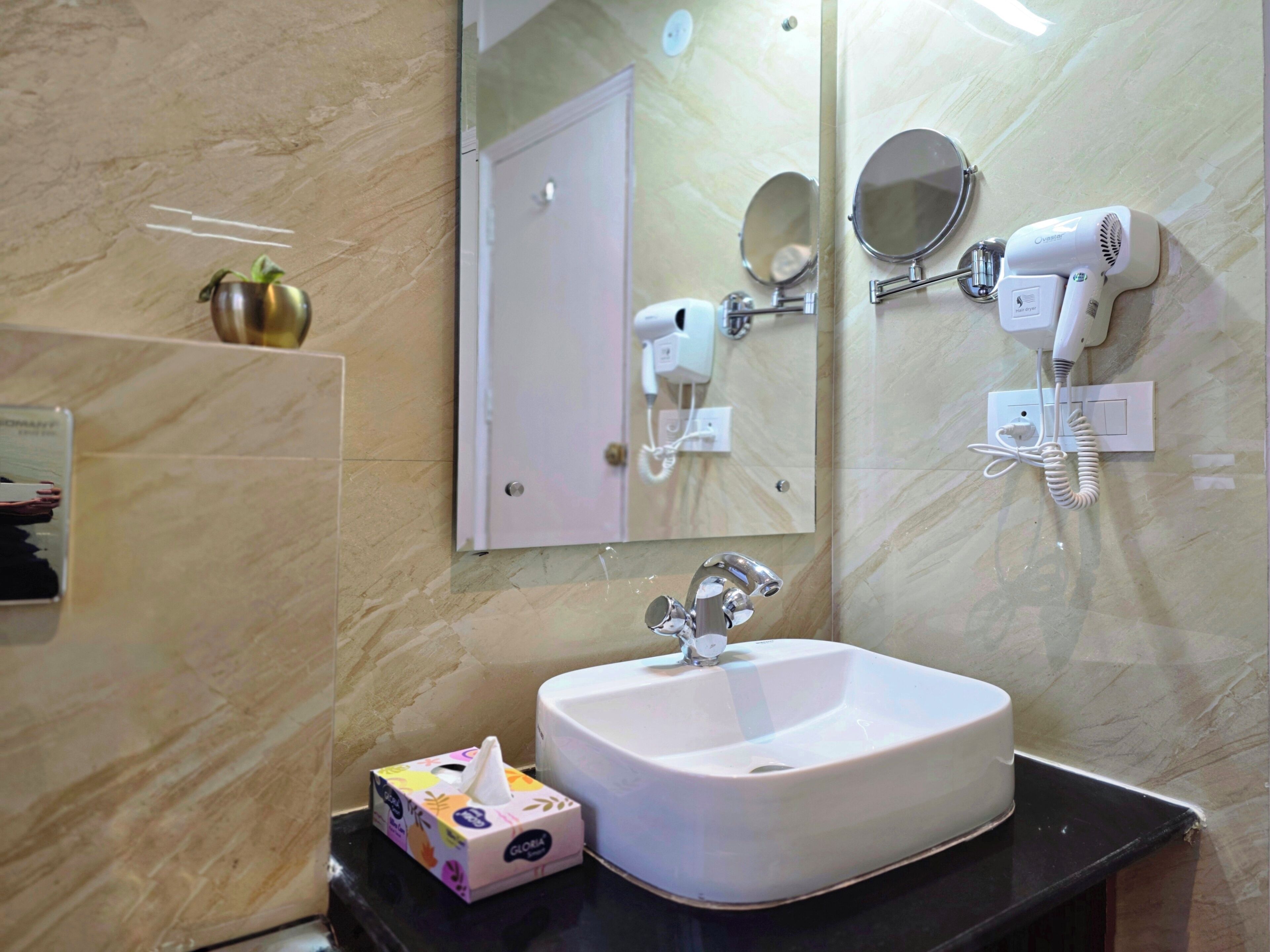 A bathroom with a white sink, a mirror, a hairdryer, and a tissue box.