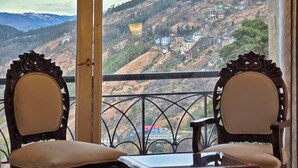 A balcony with two ornate wooden chairs and a small table, overlooking a hillside with buildings. - Shimla Golf Resorts (Shimla)