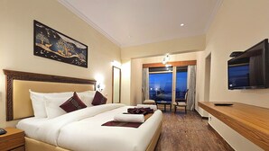 A hotel room with a large bed, a TV, a desk, and a view of the city at night. - Shimla Golf Resorts (Shimla)