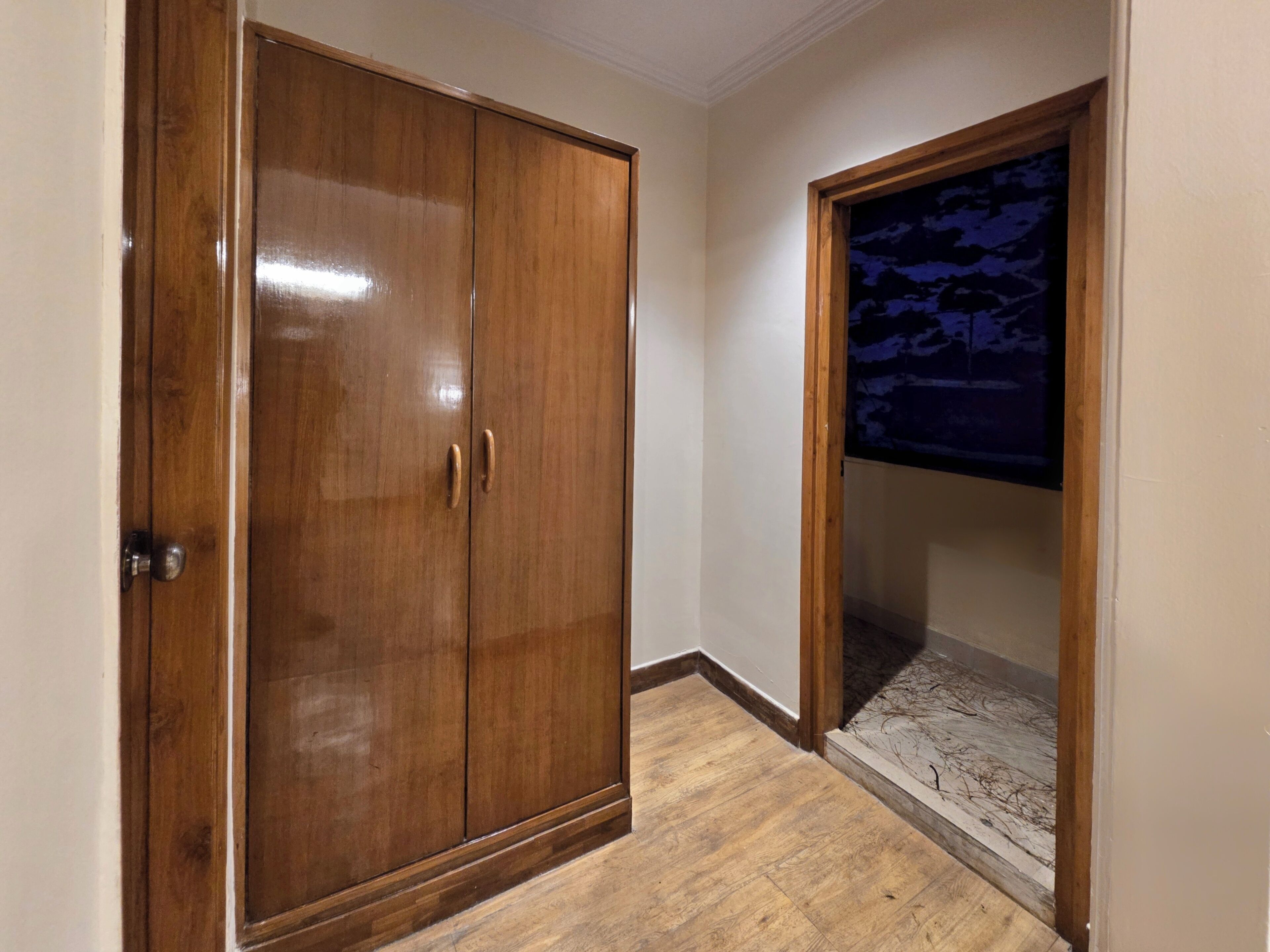 A wooden wardrobe with two doors, a wooden floor, and a wall with a window.