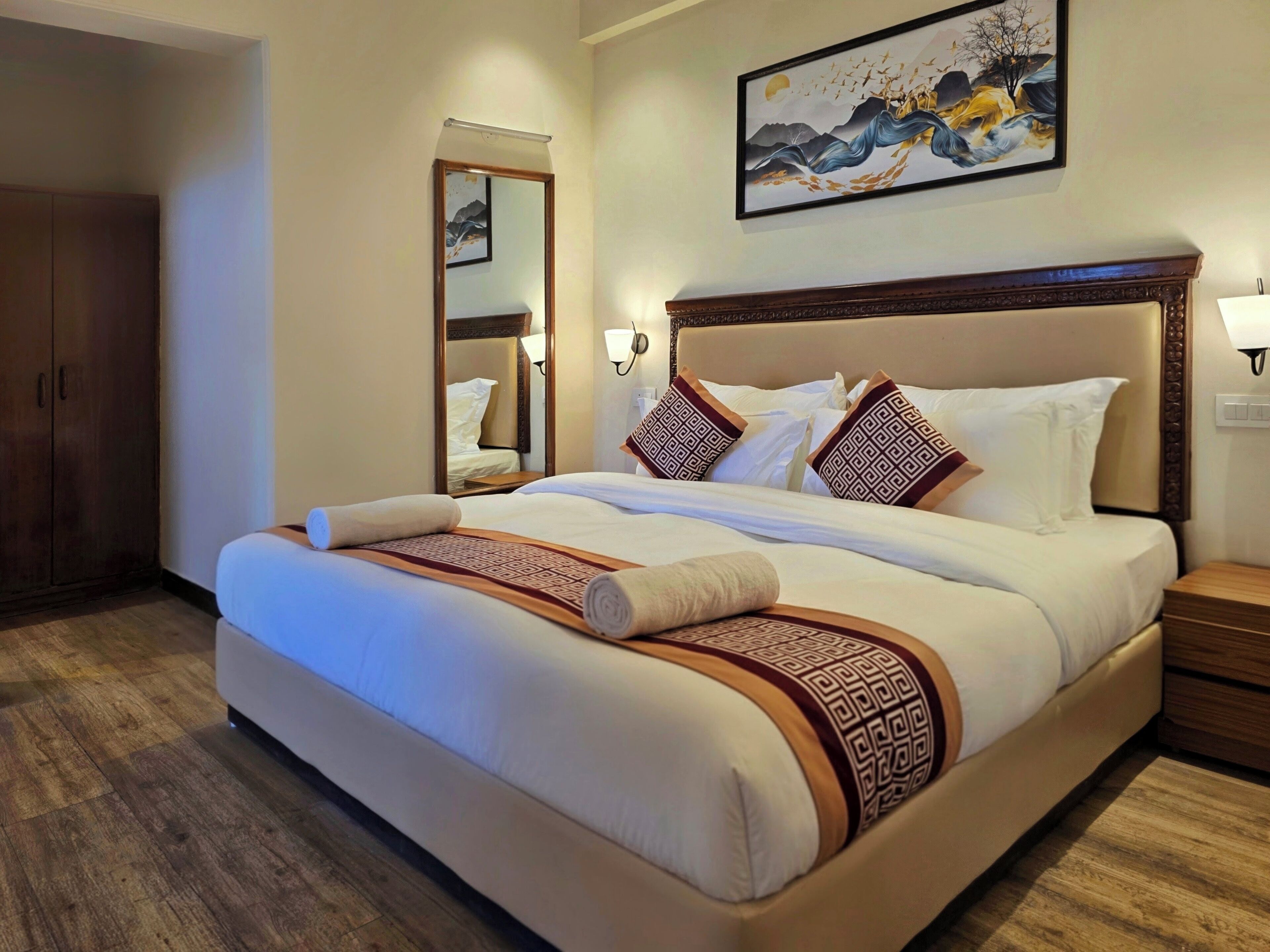 A hotel room with a large bed, wooden wardrobe, and a painting on the wall.
