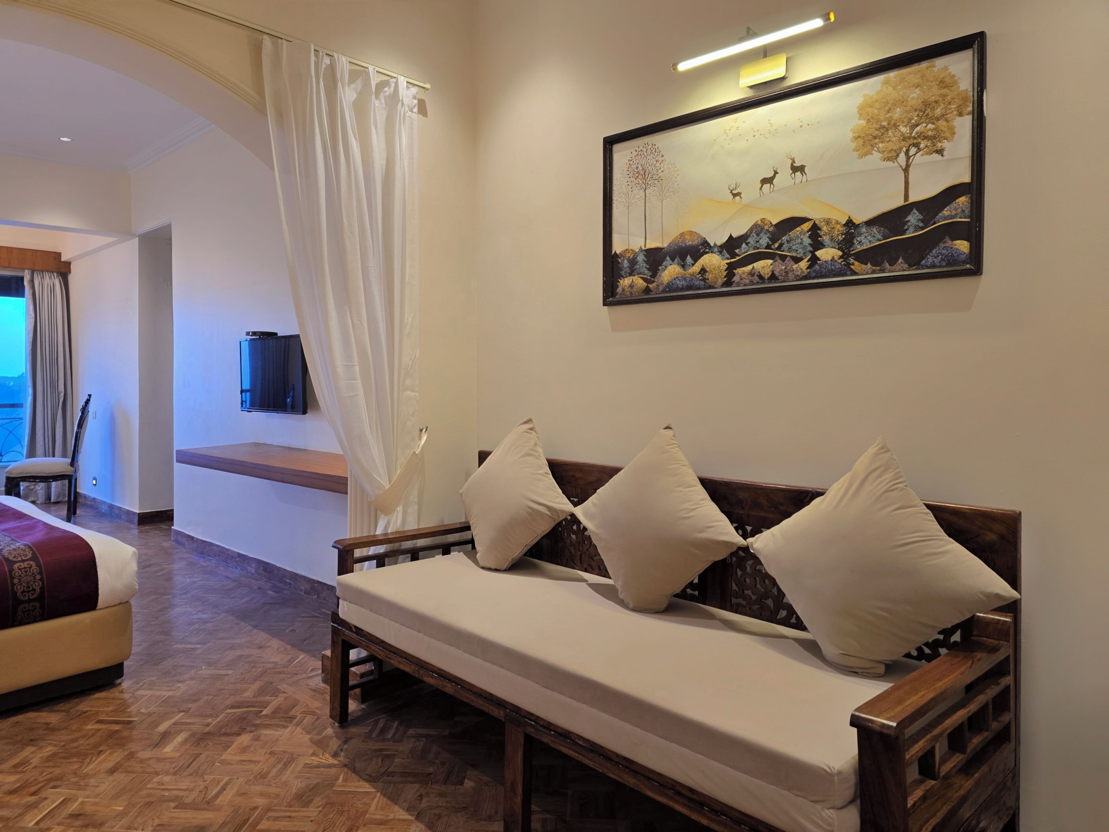 A room with a wooden bench, a TV mounted on the wall, and a painting of a landscape.