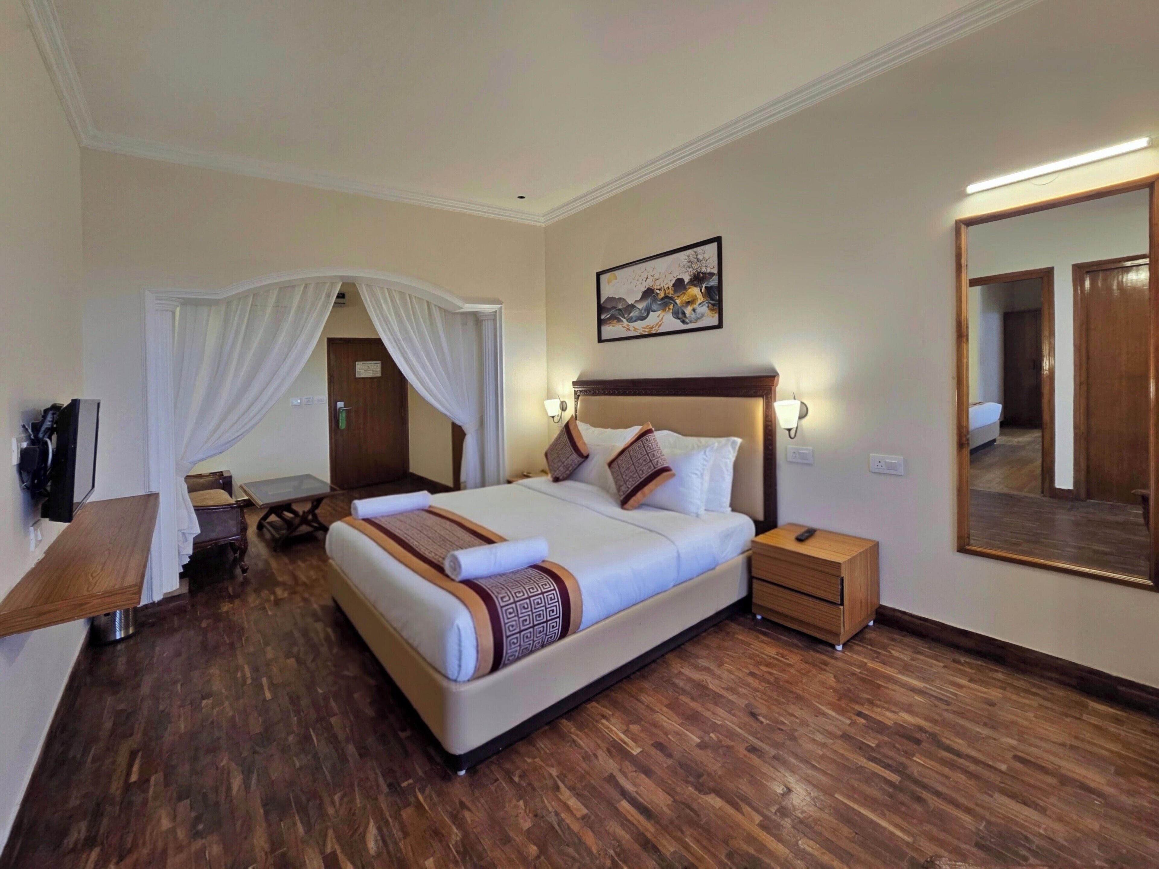 Une chambre d’hôtel avec un grand lit, des tables de chevet, un bureau, une chaise, un miroir et un luminaire au plafond.