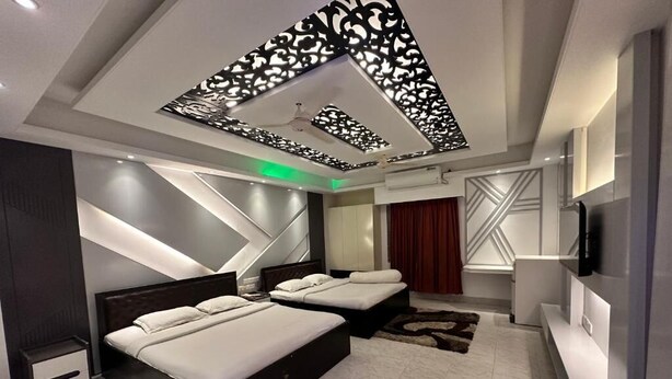A modern bedroom with two beds, a TV, and a decorative ceiling.