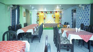 A dining area with multiple tables and chairs, a stage with floral decorations, and patterned walls.