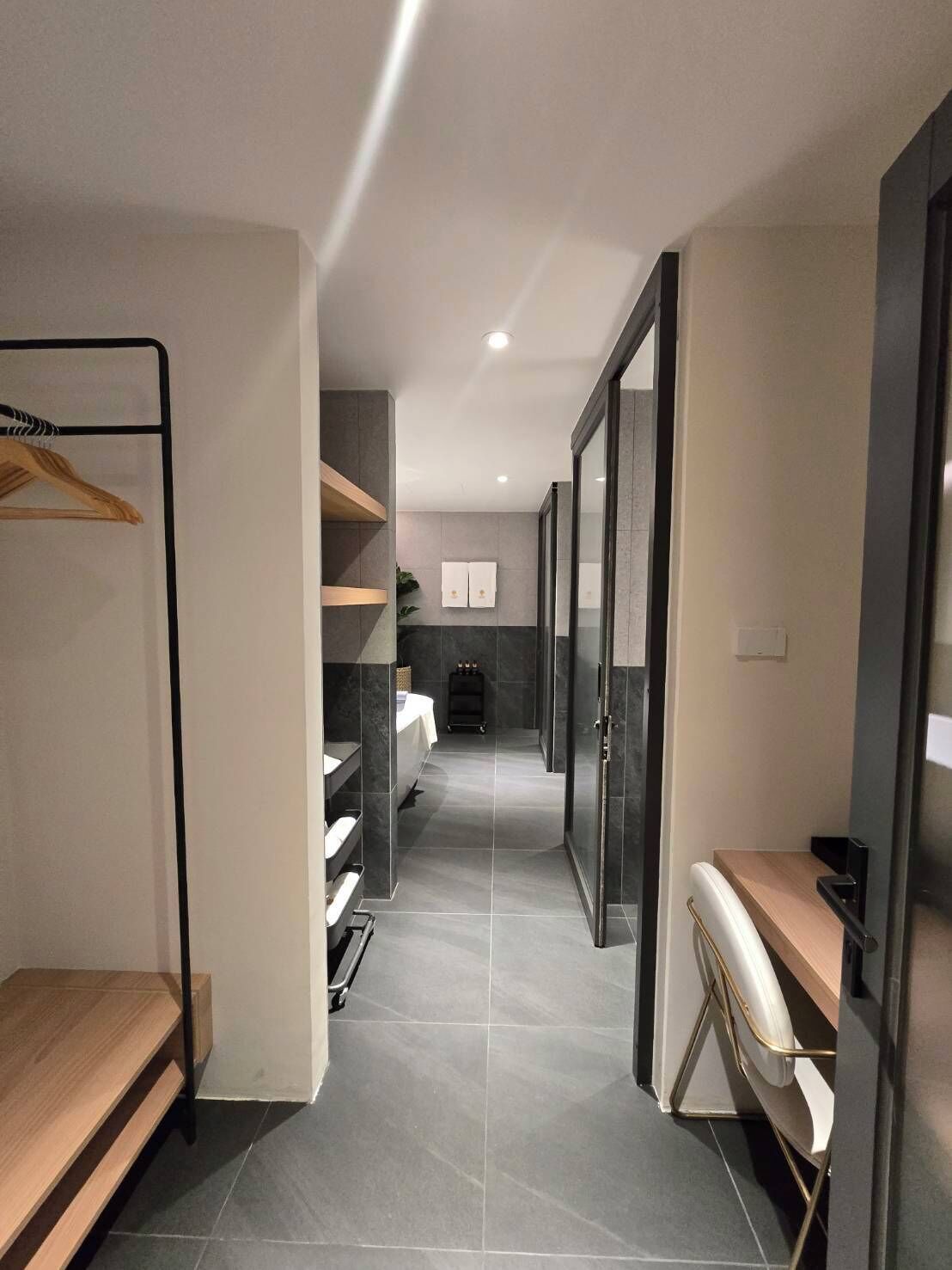 A modern bathroom with a shower, toilet, and sink. There is a wooden bench and a towel rack.