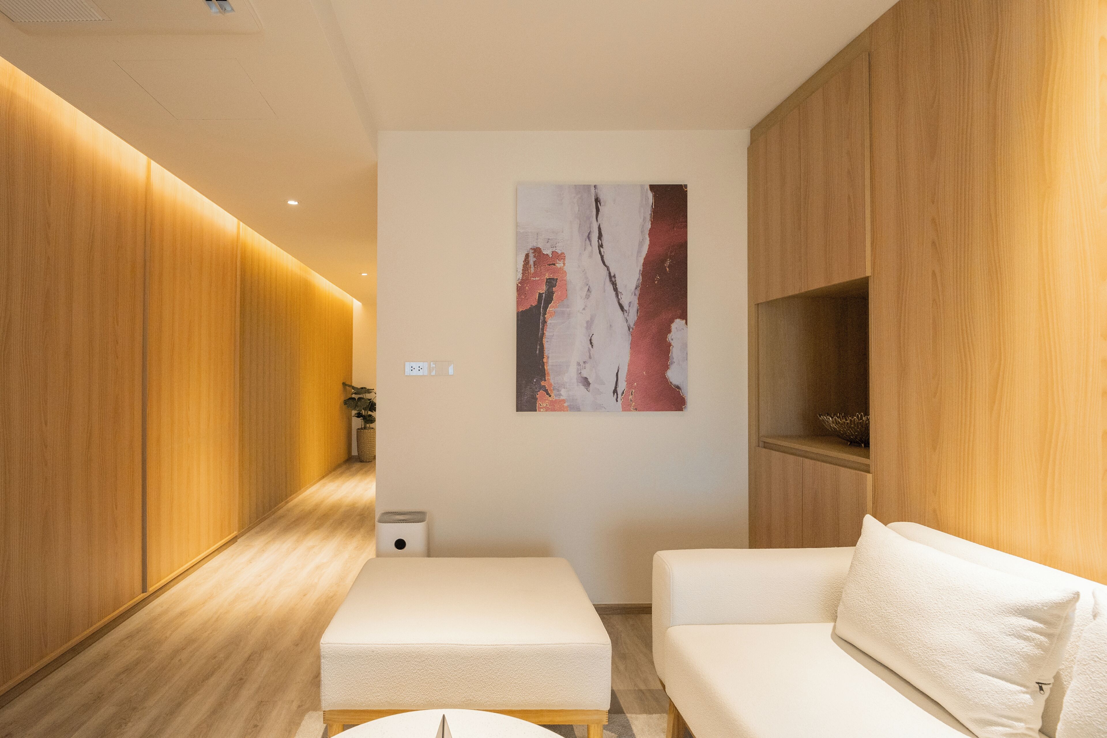 Une chambre d’hôtel moderne avec un plancher en bois, un canapé blanc, une petite table et une œuvre d’art accrochée au mur.