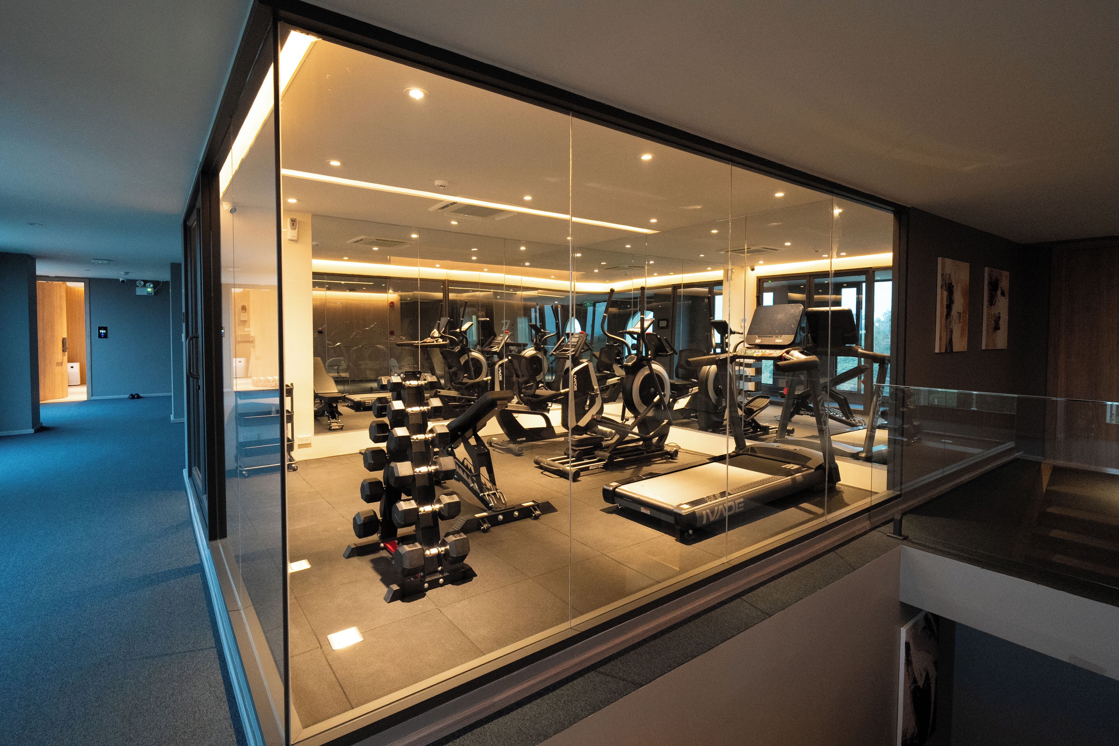 A modern gym with various exercise equipment, a glass wall, and a clean, well-lit interior.