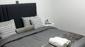 Un dormitorio moderno con cabecera oscura, almohadones a rayas y una cama bien hecha con una toalla blanca enrollada.