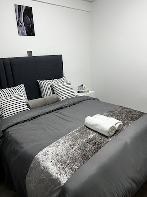 A modern bedroom with a dark headboard, striped pillows, and a neatly made bed with a rolled white towel.