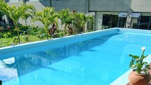 Una piscina con cubierta de madera, rodeada de vegetación y un edificio al fondo.