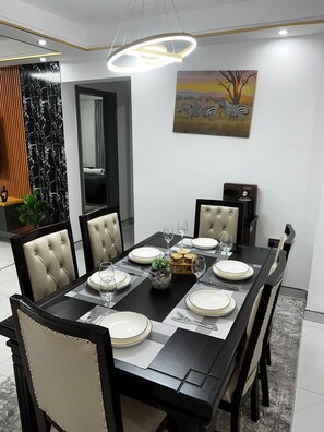 A dining room with a black table, beige upholstered chairs, and a modern pendant light.