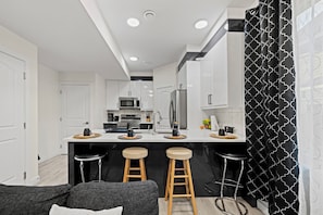 A modern kitchen with white cabinetry, stainless steel appliances, and a central island with stools.
