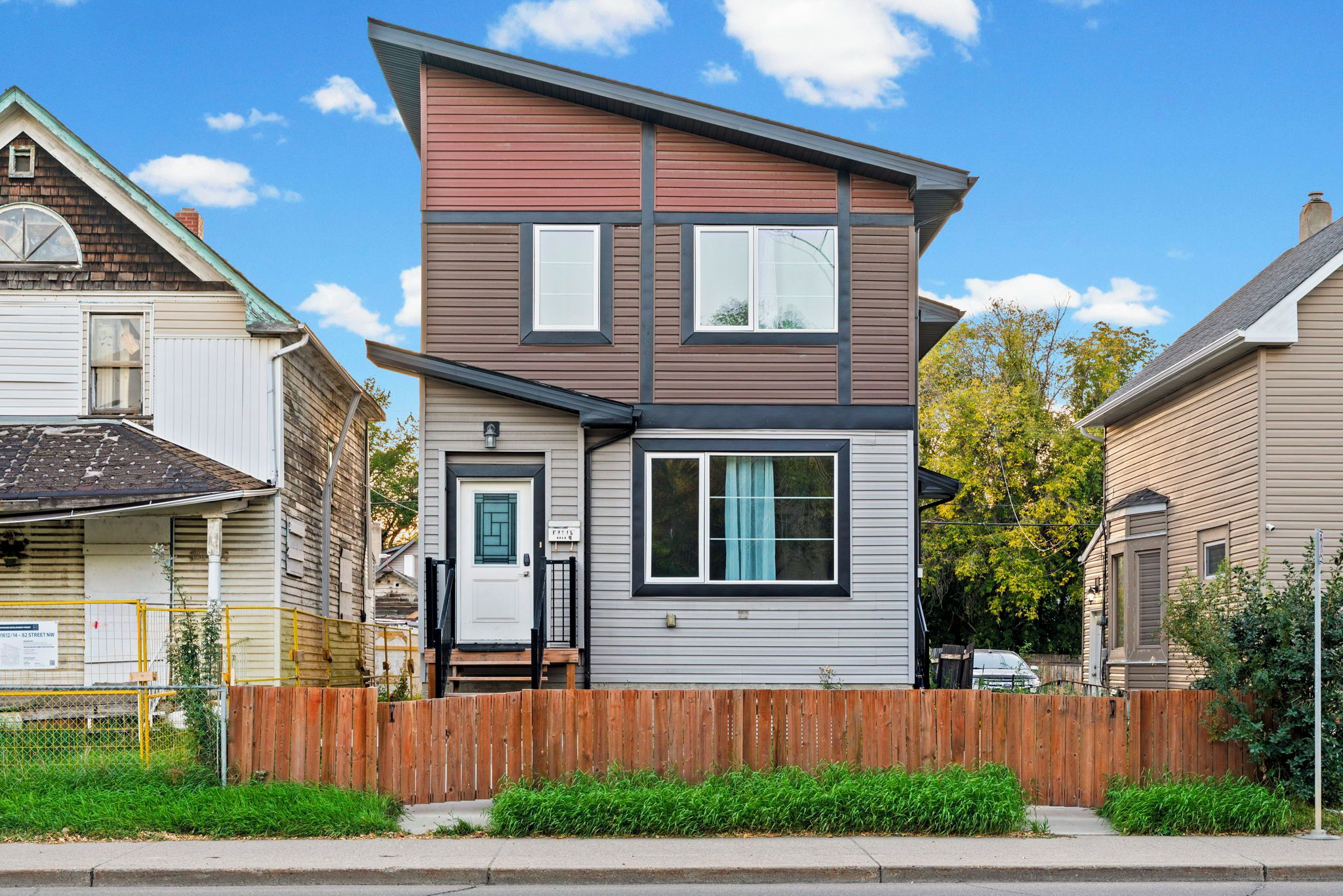A two-story residential building with a front door, a small porch, and a wooden fence.