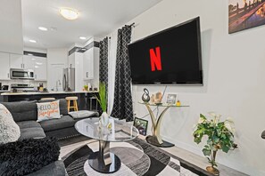 Un salon moderne avec un téléviseur à écran plat, un canapé, une table basse et une cuisine en arrière-plan.