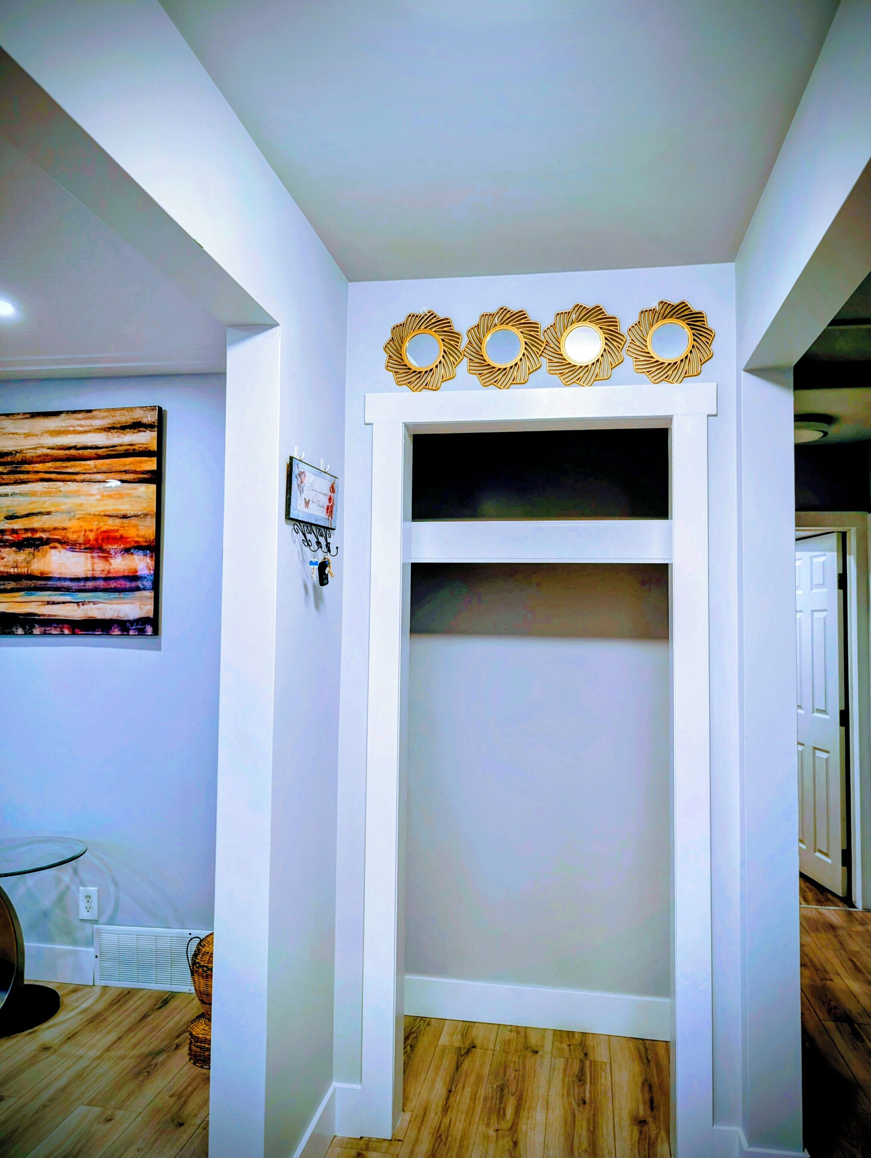 Une pièce avec un mur blanc, un grand tableau abstrait, un élément décoratif mural et une porte donnant sur une autre pièce.