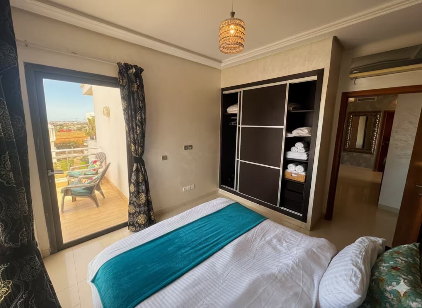 A bedroom with a bed, a wardrobe, a balcony, and a chandelier.