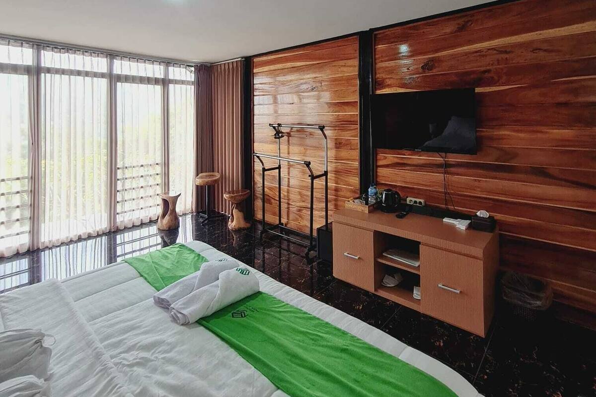 Ein Hotelzimmer mit Bett, Holzwänden, einem Fernseher, einem kleinen Hocker, einem Handtuch und einem Fenster mit Vorhängen.