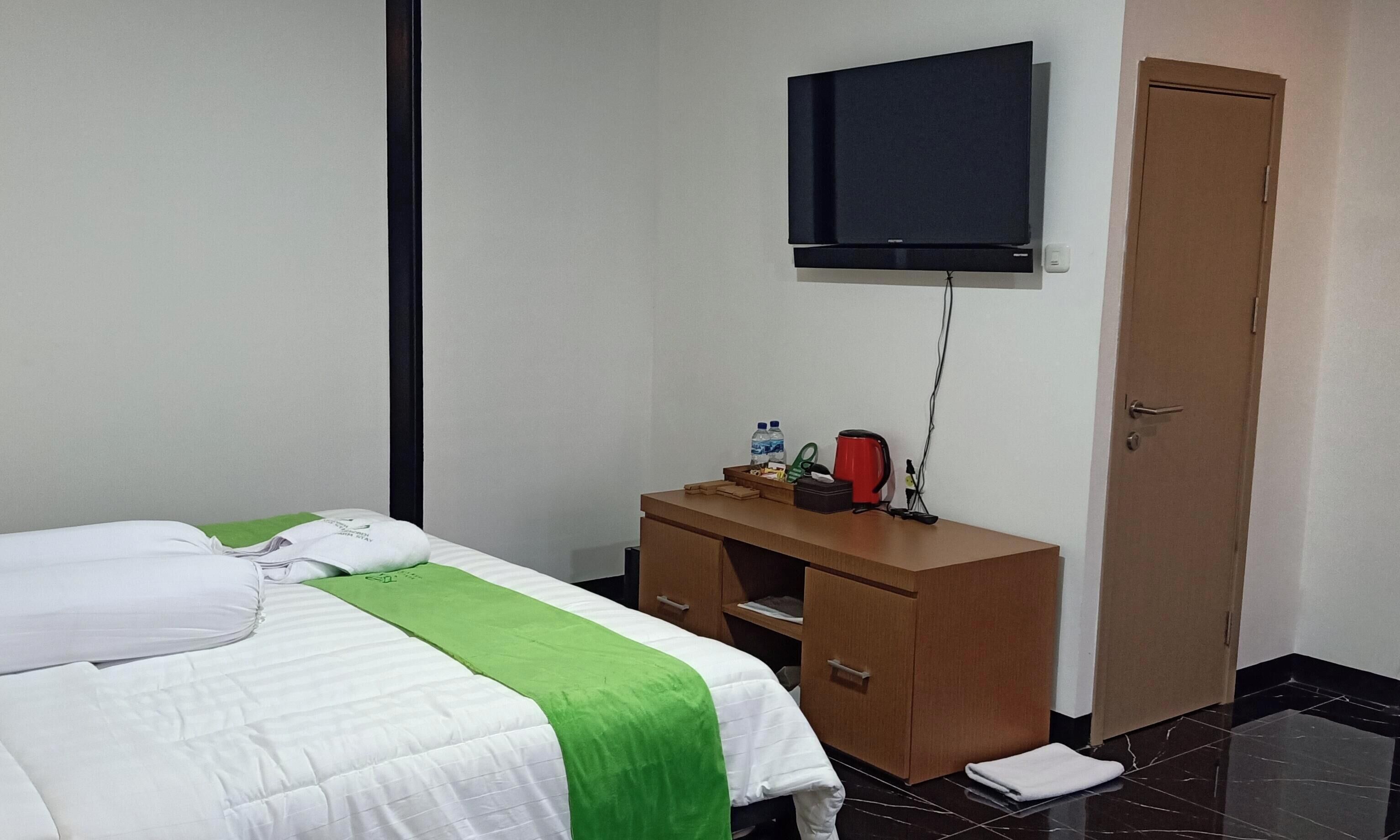 A hotel room with a bed, a wooden dresser, a television mounted on the wall, and a door.