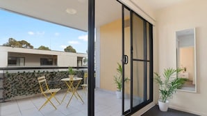 A balcony with a sliding glass door, a small table with chairs, and potted plants. - A Chic & Comfy 2BR Apt Near to Flemington Races (Melbourne)
