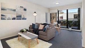 A modern living room with a sofa, coffee table, and artwork on the wall. - A Chic & Comfy 2BR Apt Near to Flemington Races (Melbourne)