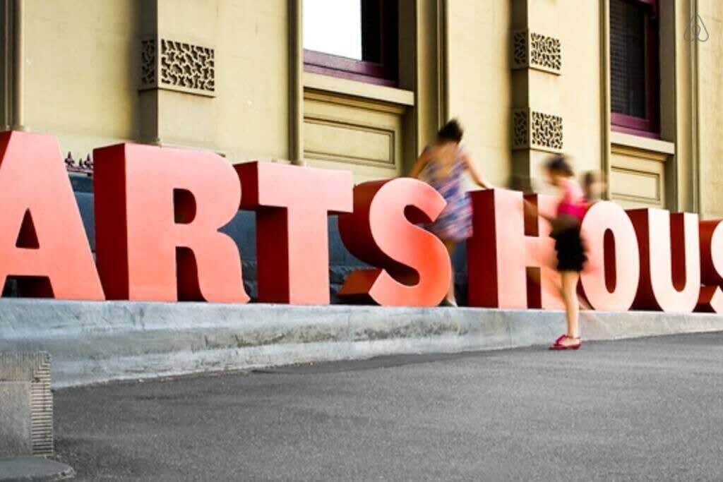 De grandes lettres rouges formant les mots « ARTS HOUSE » sont peintes sur la façade d’un immeuble.