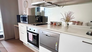 A modern kitchen with white cabinetry, a built-in oven, a dishwasher, and a coffee maker on the countertop. - Cozy Studio Apt Near Southern Cross & City Views (Melbourne)