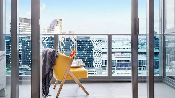 Une chambre située dans un immeuble de grande hauteur, avec une chaise jaune, un réfrigérateur Samsung et une vue sur le paysage urbain, qui comprend notamment un stade.