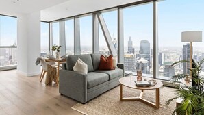Una sala de estar moderna con un sofá gris, una mesa de centro redonda y vistas de la ciudad a través de amplias ventanas.