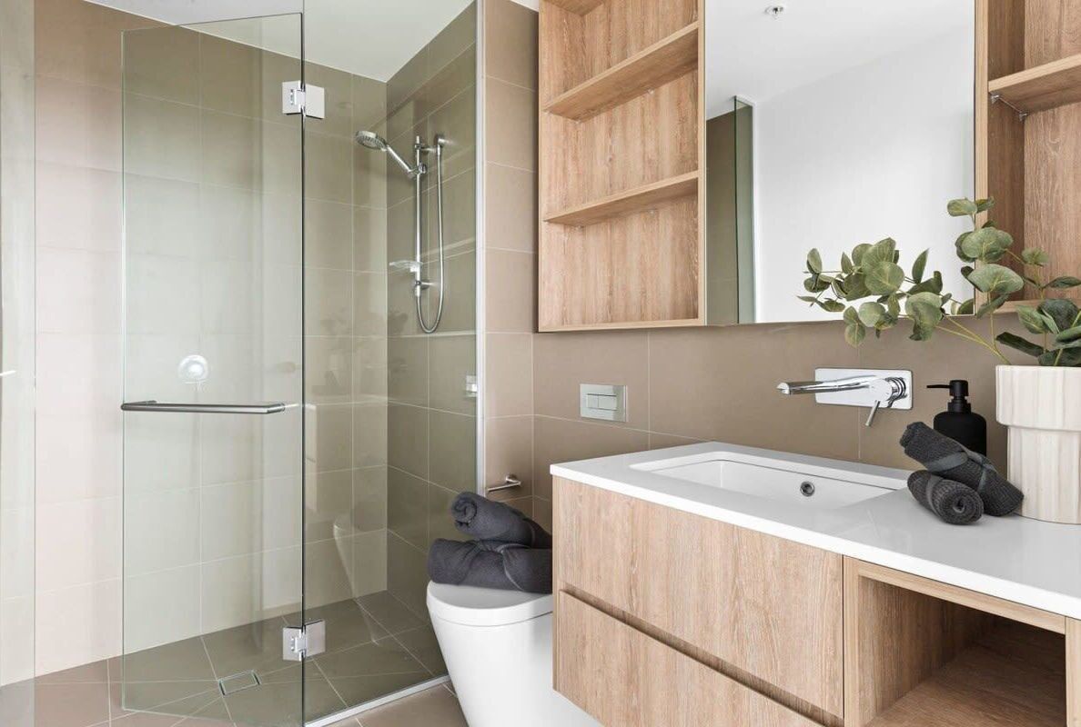 A modern bathroom with a glass shower enclosure, a white toilet, a wooden vanity with a sink, and a mirror.