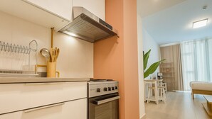 A modern kitchen with a stove, oven, and a range hood. There is a dining area with a table and chairs, and a large plant in the corner.