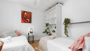 A modern bedroom with two beds, a large white wardrobe, a painting, and a small side table with a plant. - Beach house 2km CBD (South Melbourne)