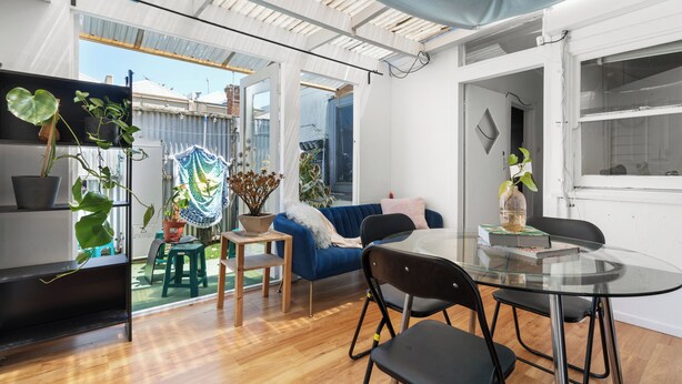 A modern living space with a glass dining table, black chairs, a blue sofa, and a variety of potted plants. - Beach house 2km CBD (South Melbourne)