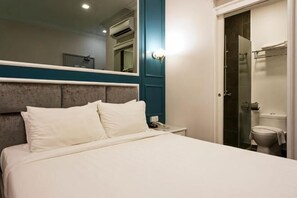 Et hotelværelse med en seng, et natbord, et spejl og et badeværelse med toilet og bruser.