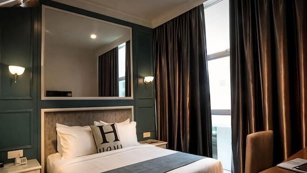 A hotel room with a large bed, a nightstand, a chair, a desk, a mirror, and a window with curtains. - H Boutique Hotel Sri Petaling (Kuala Lumpur)