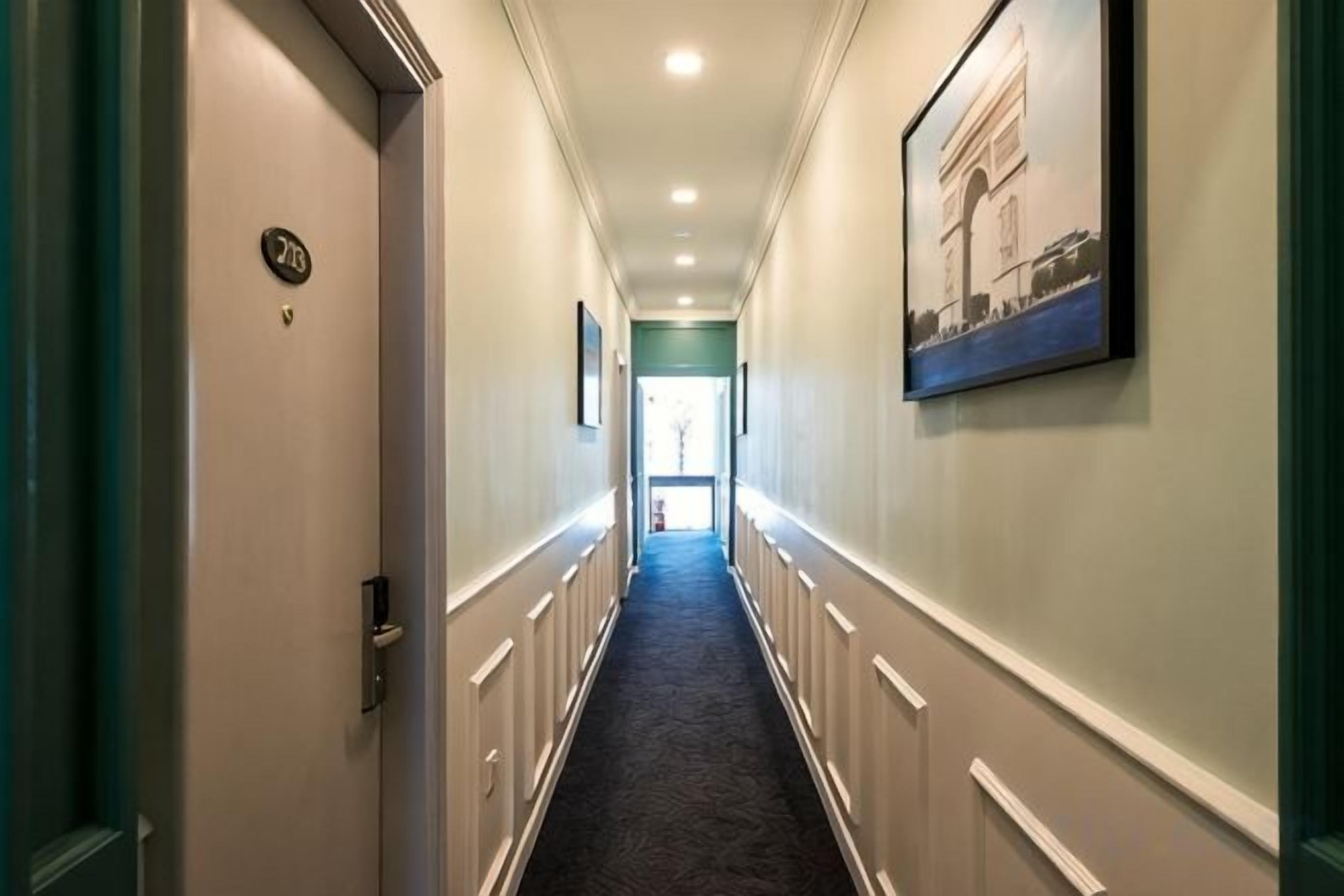 A hotel corridor with a door labeled '3B', a framed picture on the wall, and a carpeted floor.