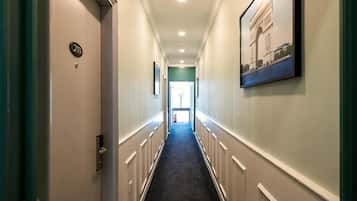 Een hotelgang met een deur waarop '3B' staat, een ingelijst kunstwerk aan de muur en een vloerbedekking.