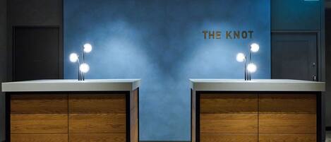 A modern bathroom with two wooden vanity units, each with a mirror and three lights. The wall behind the vanities is painted blue, and the text "THE KNOT" is visible.