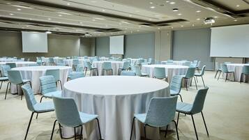 A conference room with multiple round tables, each surrounded by chairs, and a large screen at the front.
