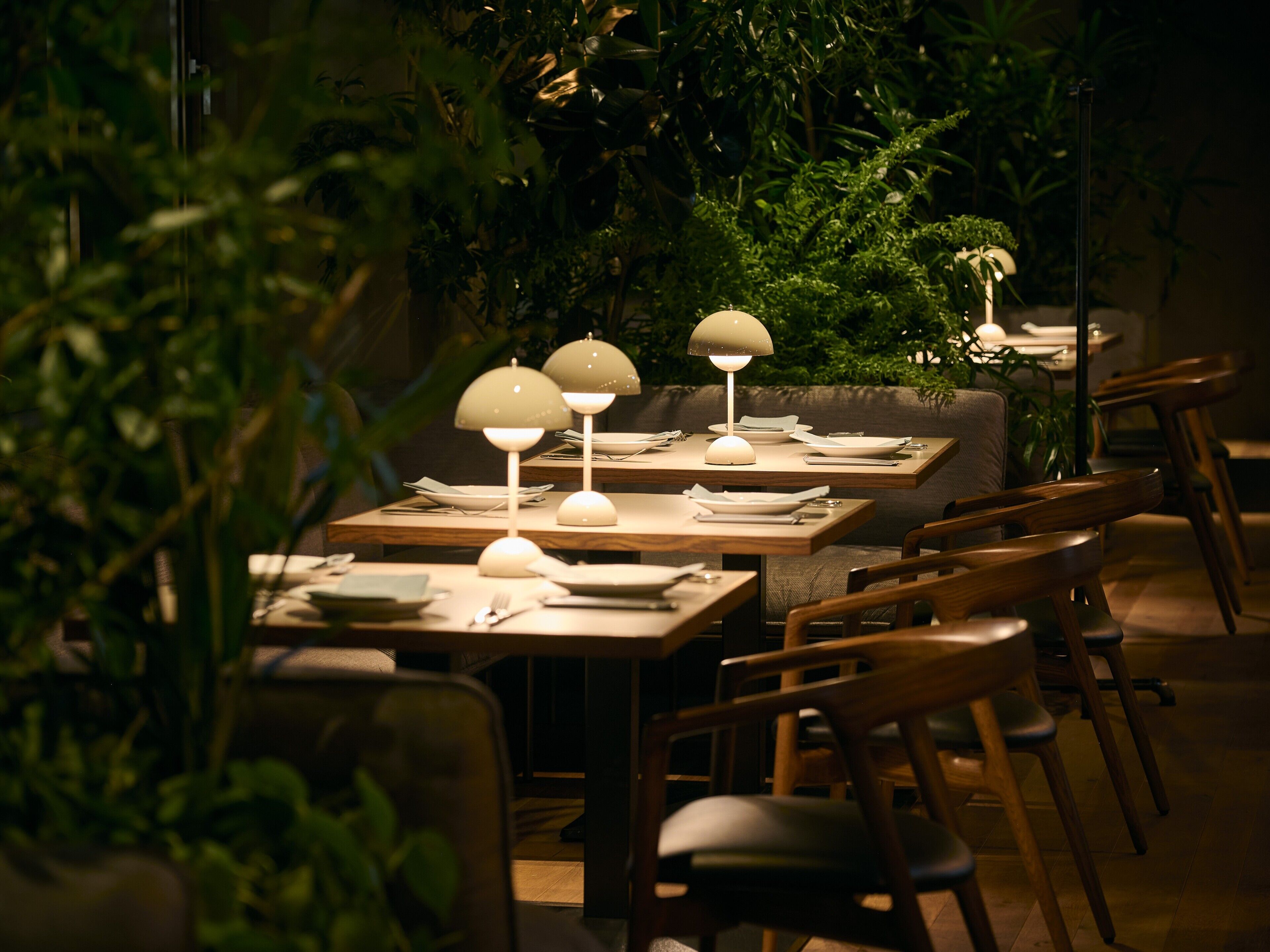 Ein Restaurant mit gedeckten Tischen, umgeben von viel Grün.