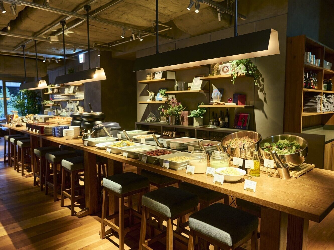 A long communal dining area with multiple barstools, a variety of food stations, and shelves with decorative items.