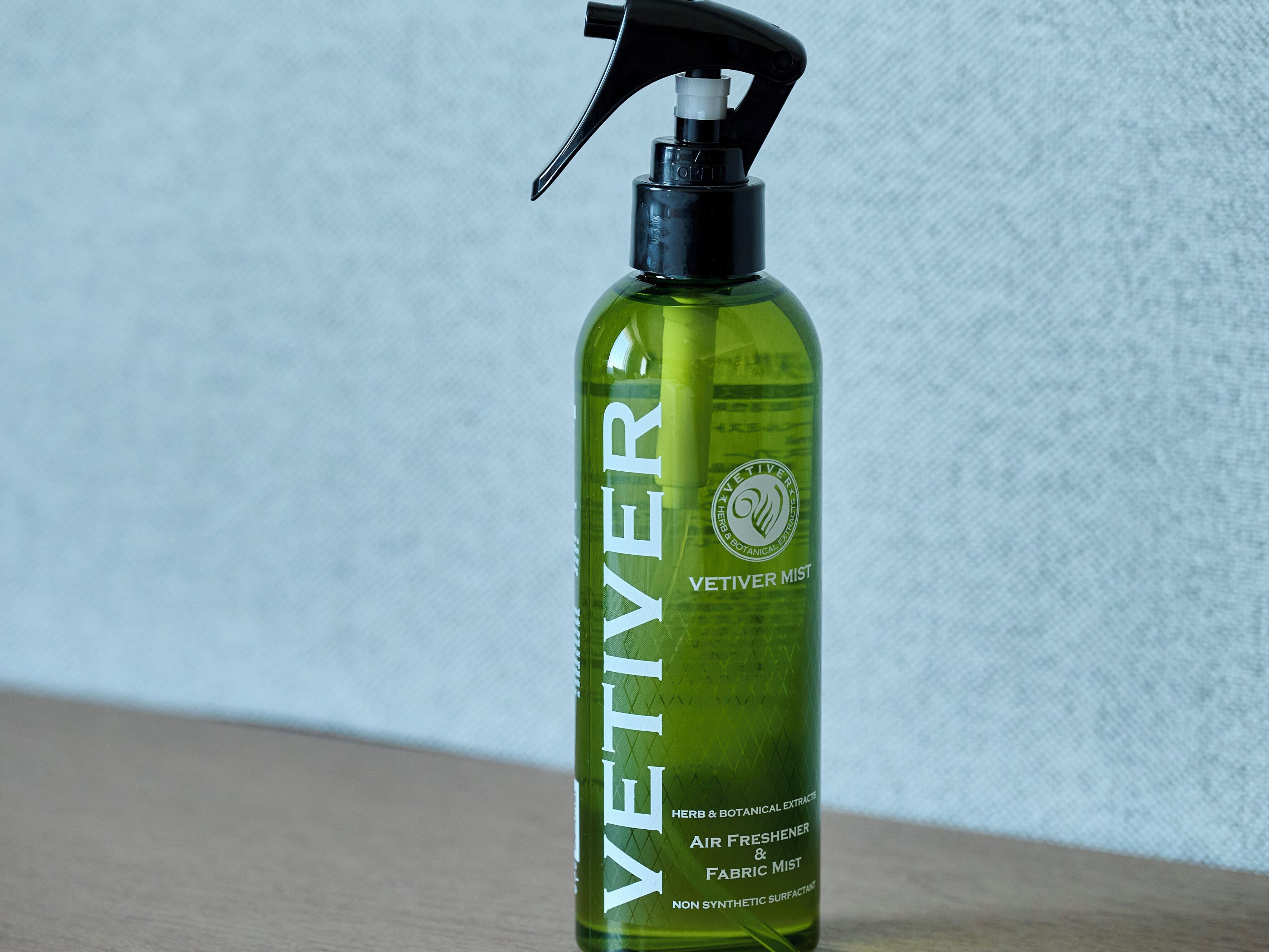 Vihreä VETIVER-tuoksusuihkeen pullo, jossa on pumppumekanismi, ja jossa lukee, että se on synteettisiä aineita sisältämätön tekstiilien raikastin.