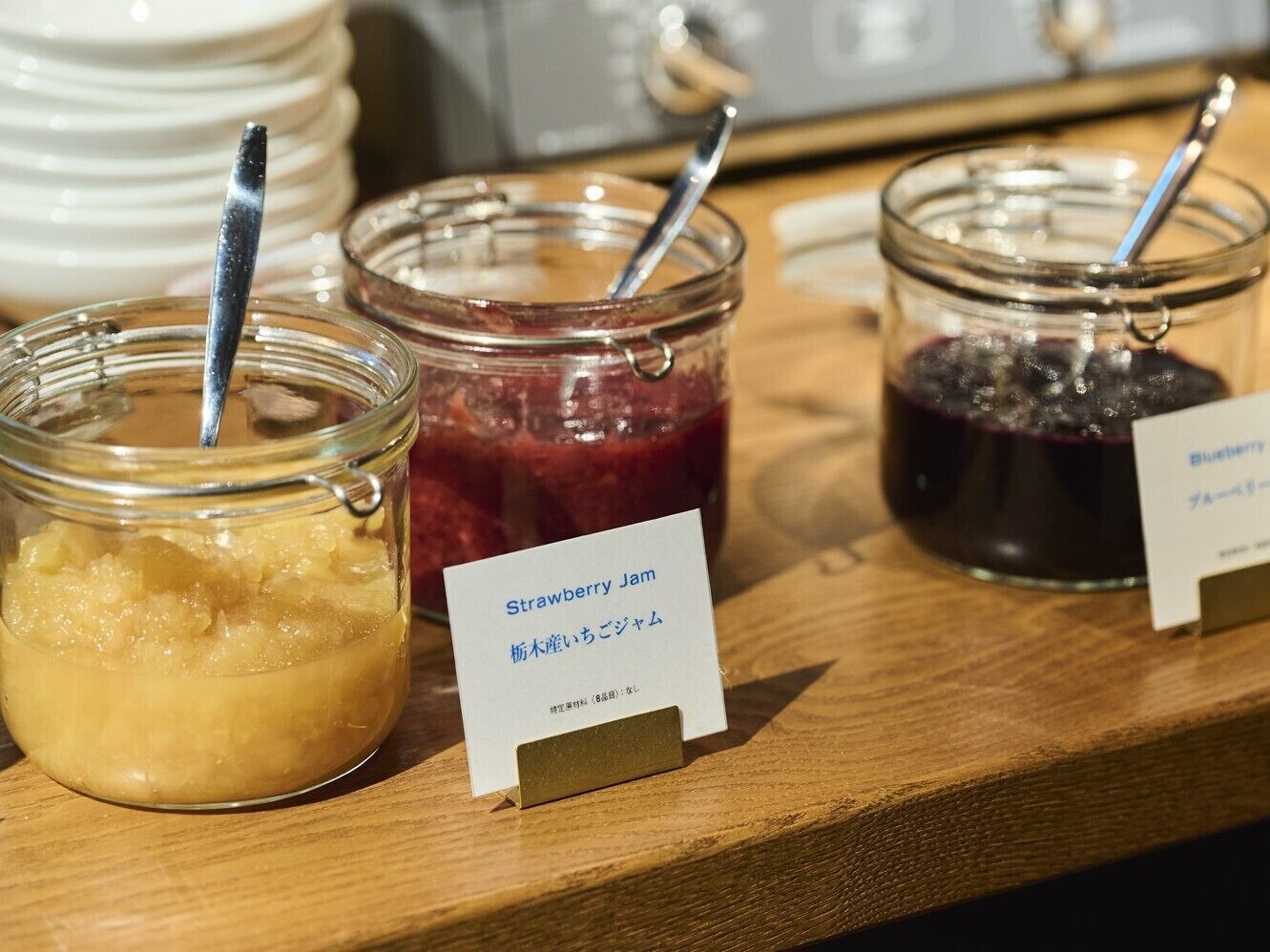 Tres frascos de mermelada con etiquetas, uno etiquetado 'Strawberry Jam', sobre una superficie de madera.