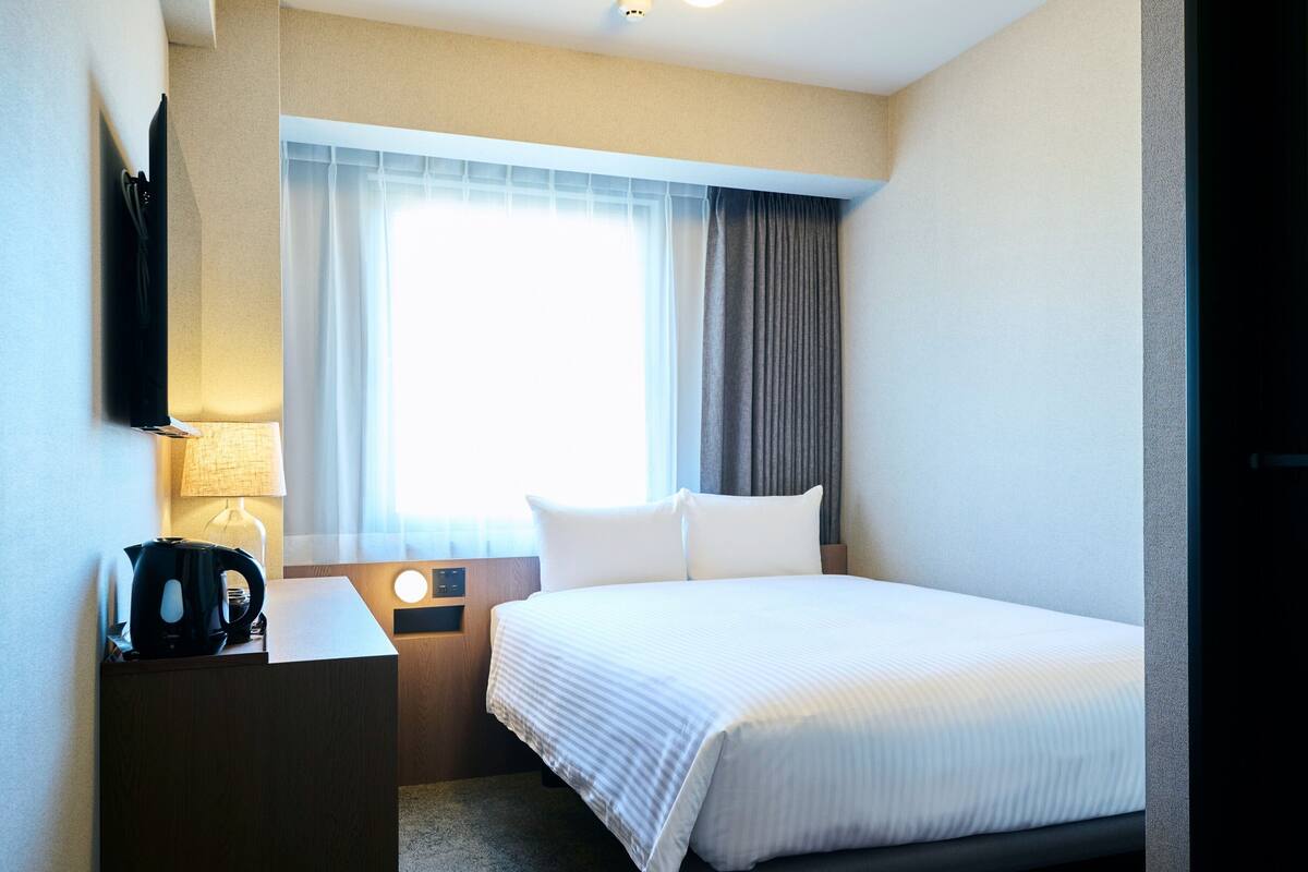 Ein Hotelzimmer mit einem Bett, einem Schreibtisch, einer Lampe und einem fenster mit Vorhängen.