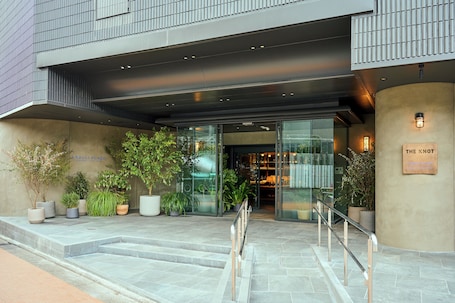A modern building entrance with a glass facade, outdoor seating area, and a sign reading "THE KNOT".