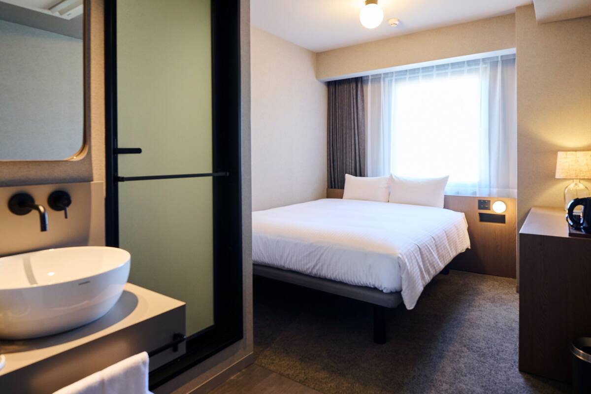 Ein Hotelzimmer mit einem großen Bett, einem Badezimmer mit Waschbecken und einem Fenster mit Vorhängen.
