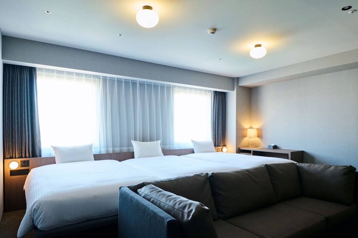 Ein modernes Hotelzimmer mit einem großen Bett, einer Couch und einem Schreibtisch mit Lampe.